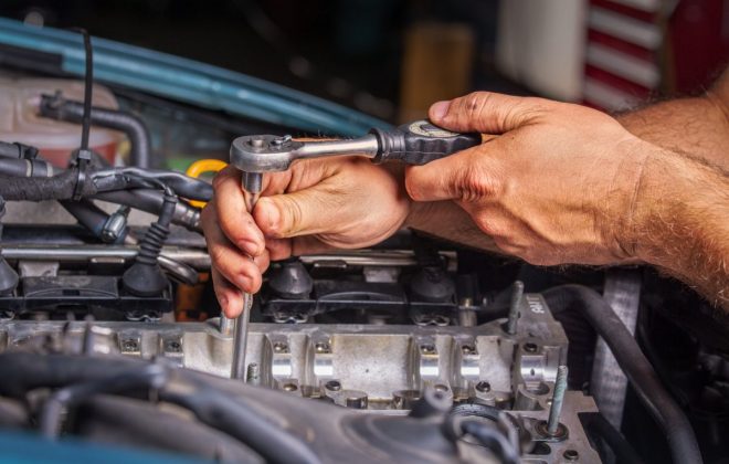 Mains du garagiste resserrant une culasse avec un cliquet et une rallonge de quinze