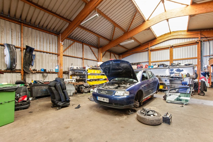 Intérieur d'un local de garage avec voiture au capot ouvert et sans roue.