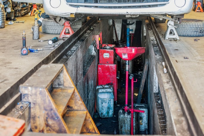 Vue sur une fosse de garage sous une voiture avec des équipements de garagiste.