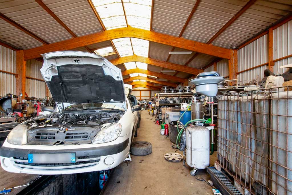 Intérieur de la casse automobile avec vue sur un capot ouvert de voiture et des rayonnages de pièces auto.